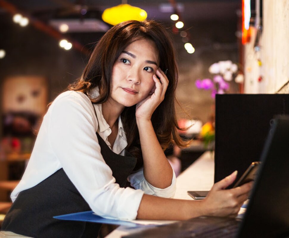 Frau mit samtenem Blick, sitzend am Tisch, konzentriert auf einen Laptop in einem stilvollen, beeinträchtigten Café.