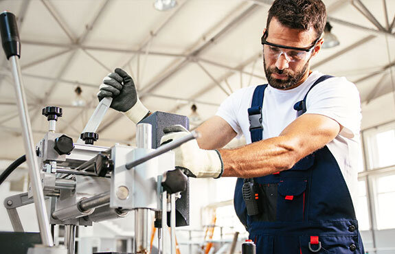 Mechaniker arbeitet konzentriert an einer Präzisionsmaschine in einer hellen Werkstatt. Schutzbrille und Handschuhe getragen.