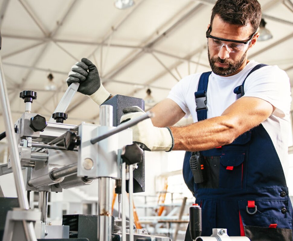 Mann in Arbeitskleidung bedient eine Maschine in einer modernen Werkstatt, umgeben von Werkzeugen und Maschinen.