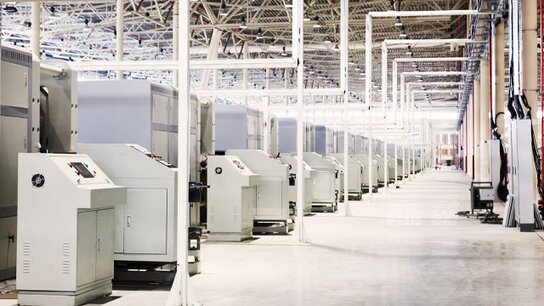 Reihe moderner Maschinen in einer hellen Industriehalle mit hohen Decken und sichtbaren technischen Steuerungen.