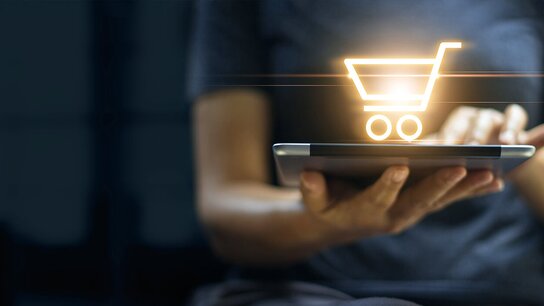 Eine Person hält ein Tablet mit einem leuchtenden Einkaufswagen-Symbol, das Einkaufsaktivität symbolisiert.