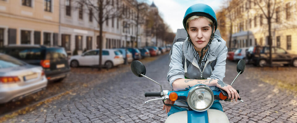 Junge Person auf einem Roller in einer urbanen Umgebung mit gepflasterter Straße und parkenden Autos im Hintergrund.