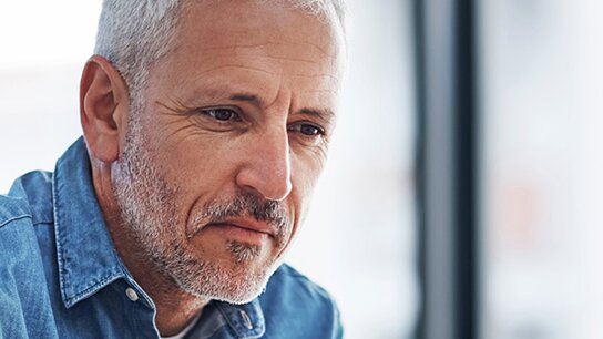 Mann mittleren Alters mit grauen Haaren, der konzentriert an einem Laptop arbeitet, in einem hellen Raum.